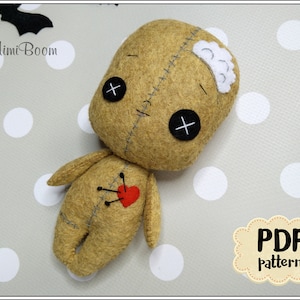May include: A brown felt voodoo doll with black eyes, a red heart, and stitches. The doll has a white felt patch on its head. The doll is lying on a gray and white polka dot background. PDF pattern.