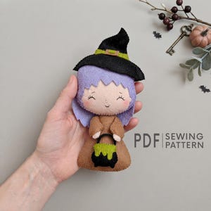 May include: A felt witch doll featuring lavender hair, a black pointed hat with a green band, and a brown dress. The doll holds a small black cauldron with green liquid inside. The text PDF SEWING PATTERN is printed on the right side.