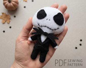 May include: A small, handmade felt doll featuring a white, round head with large black oval eyes and a stitched mouth. The doll wears a black felt suit with a matching bow tie. The text PDF SEWING PATTERN is printed in the bottom right corner.