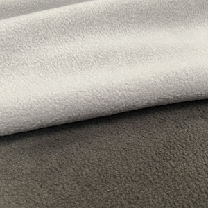 Könnte beinhalten: Nahaufnahme von zwei Stücken Fleece-Stoff. Ein Stück ist hellgrau und das andere dunkelgrau.