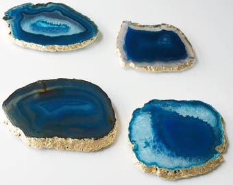 May include: Four blue agate coasters with gold trim. The coasters are round and have a natural, organic shape.