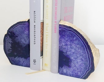 May include: Purple agate bookends with a natural, rough edge, holding several books. The bookends have a polished, crystalline interior. The books include titles like "made" and "The Little Dictionary of Fashion".