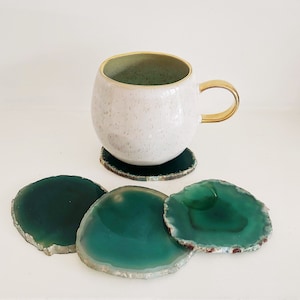 May include: Set of four green agate coasters with a white ceramic mug with a gold rim and handle on top of one of the coasters.
