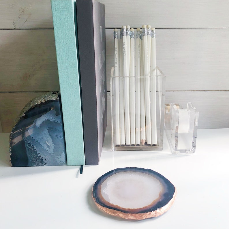 May include: A set of white pencils in a clear acrylic holder, a blue and green book, a blue and grey agate bookend, and a white agate coaster.
