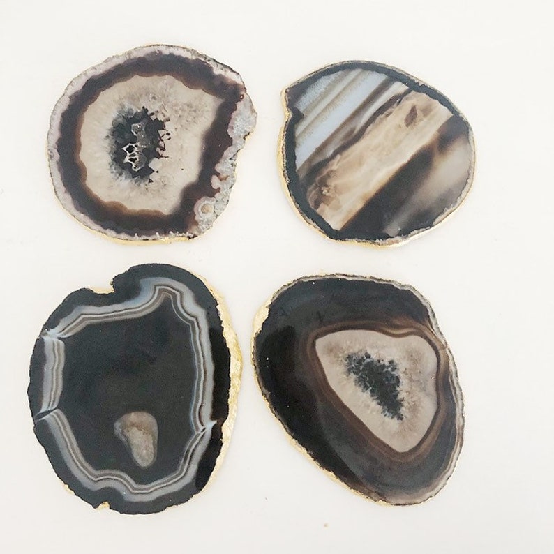 May include: Four agate coasters with gold trim. Each coaster features a unique pattern of black, white, and brown agate.