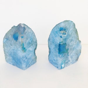 May include: Two blue agate bookends with a white background. The agate is translucent and has a natural crystal formation.