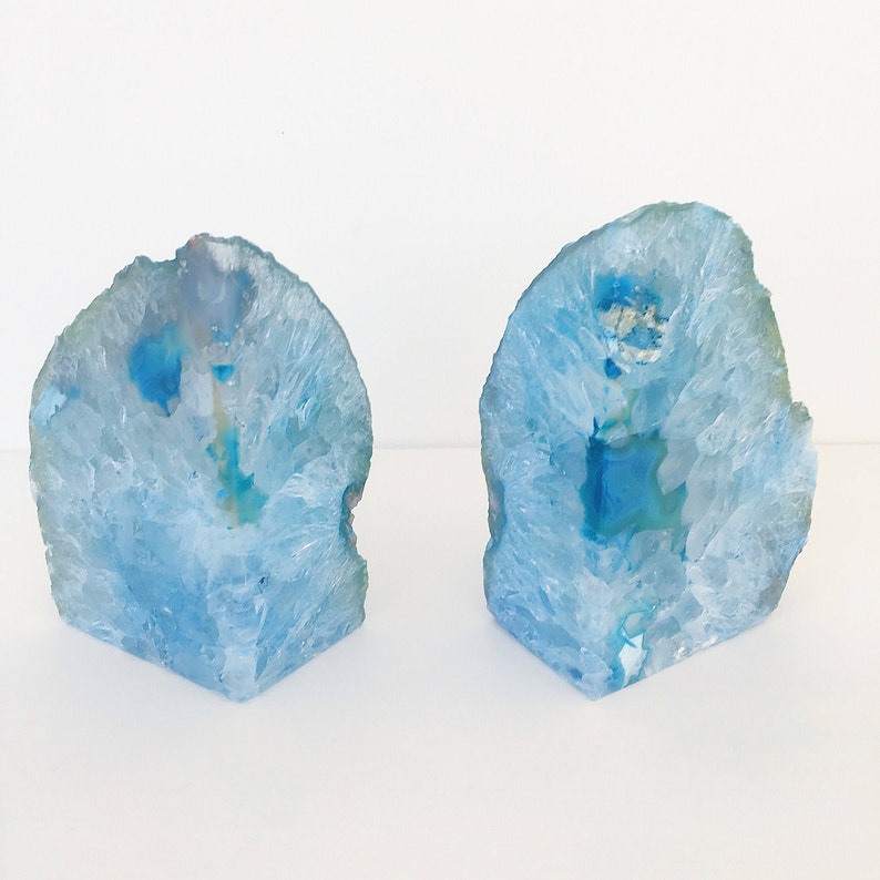 May include: Two blue agate bookends with a white background. The agate is translucent and has a natural crystal formation.