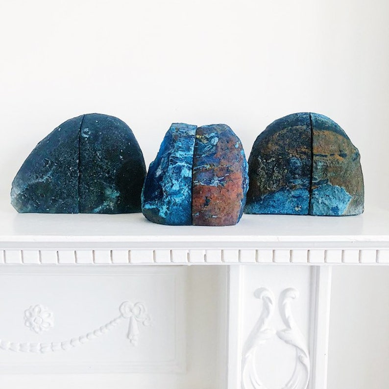 May include: Three blue agate bookends with a natural, rough-hewn finish. The bookends are shaped like a mountain range and have a unique, swirling pattern of blue, green, and brown.