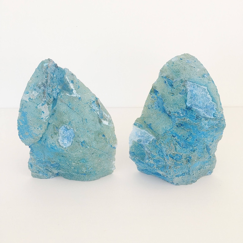 May include: Two blue and green agate bookends with a rough, natural texture. The bookends are shaped like small, irregular rocks.