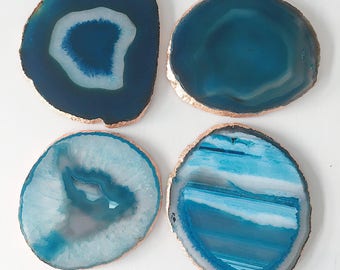 May include: Four natural agate coasters in shades of blue and white, with a metallic gold edge. The coasters have unique patterns and shapes, perfect for adding a touch of elegance to any home decor.