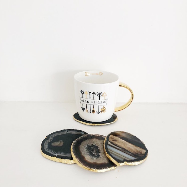 May include: Four black and gold agate coasters with a white mug with black and gold arrows and the text "wild within" on it.