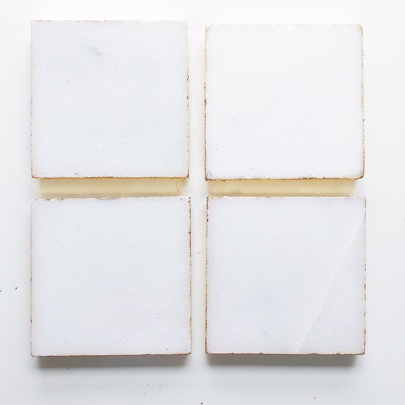 May include: Four white square tiles with a slightly rough texture and a subtle gold border.