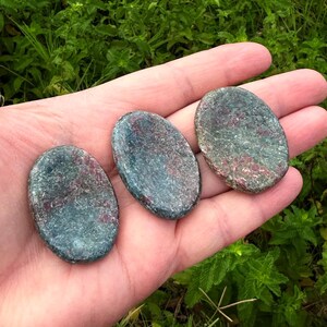 Könnte beinhalten: Drei oval geformte Steine mit einer glatten, polierten Oberfläche. Die Steine weisen ein gesprenkeltes Aussehen mit einer Mischung aus tiefen waldgrünen, blaugrünen und rötlich-kastanienbraunen Mineraleinschlüssen auf ihren flachen, runden Formen auf.