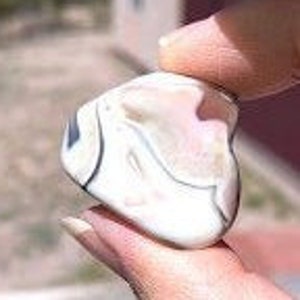May include: A white agate stone with black and gray banding. The stone is smooth and polished, with a heart-shaped outline.