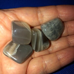 May include: Four gray and white moonstone tumbled stones. The stones are smooth and polished.