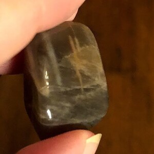 May include: A smooth, gray and white gemstone with a unique pattern. The stone is tumbled and has a polished finish.