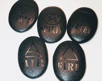 May include: Five black oval-shaped stones with different symbols and words engraved on them. The words are "EARTH", "SPIRIT", "WATER", "AIR", and "FIRE".