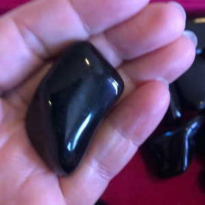 May include: A collection of black obsidian tumbled stones. The stones are smooth and polished, with a glossy finish.