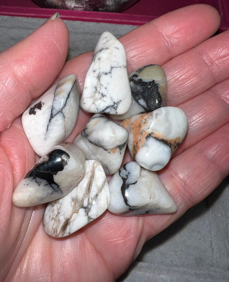 Peut inclure: Une collection de huit pierres blanches roul&eacute;es avec des veines noires et brunes. Les pierres sont lisses et polies, et elles ont un aspect naturel et organique.