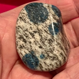 May include: A smooth, polished, gray and white stone with blue, swirling patterns. The stone is a natural, tumbled, polished rock.