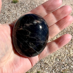 May include: A smooth, black, polished stone with a striated pattern. The stone is round and has a glossy finish.