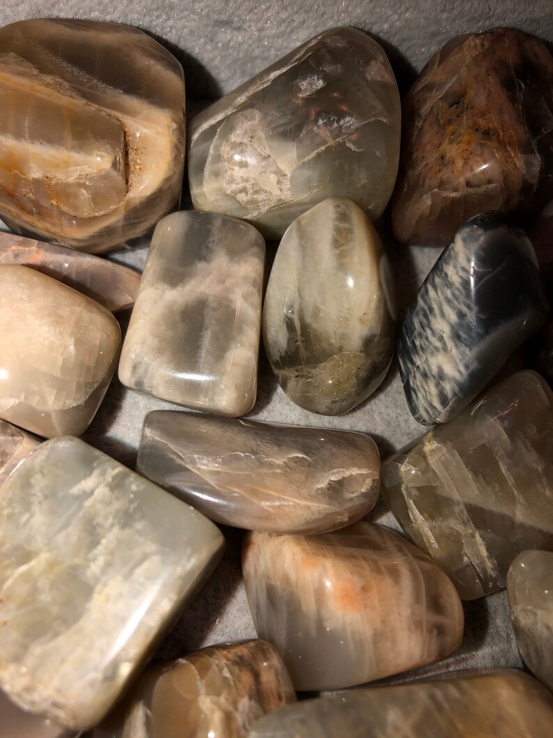 May include: A collection of smooth, polished moonstone stones in various shades of gray and white. The stones are tumbled and have a natural, organic look.