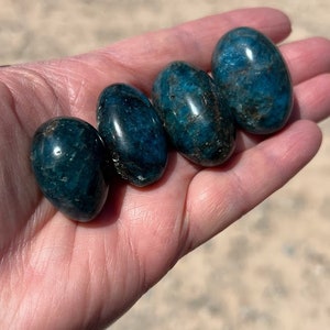 Puede incluir: Cuatro piedras lisas de apatita azul de forma ovalada. Las piedras son de color azul intenso con un ligero brillo.