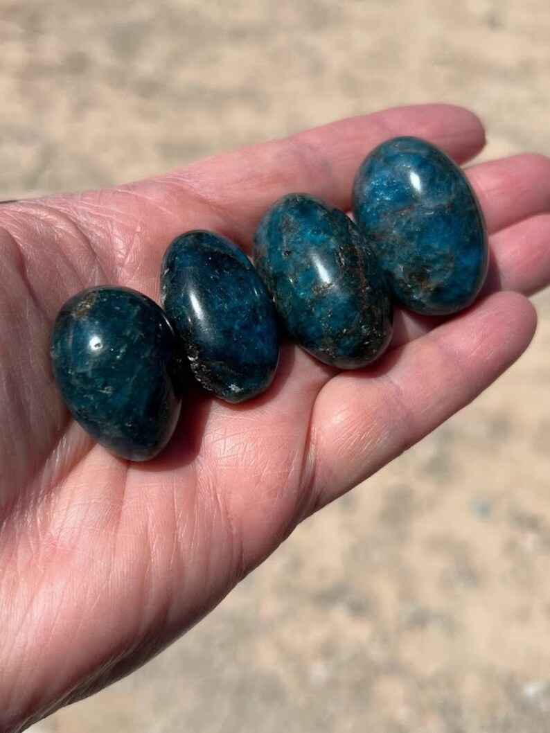 Puede incluir: Cuatro piedras lisas de apatita azul de forma ovalada. Las piedras son de color azul intenso con un ligero brillo.
