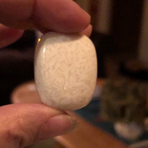 May include: A white oval-shaped stone with a swirling pattern of thin, light brown lines.