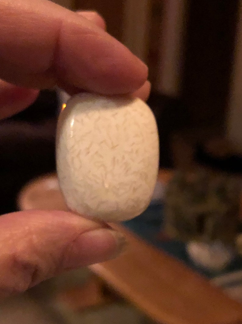 May include: A white oval-shaped stone with a swirling pattern of thin, light brown lines.