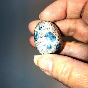 May include: A smooth, oval-shaped blue and white kyanite stone with a speckled pattern.