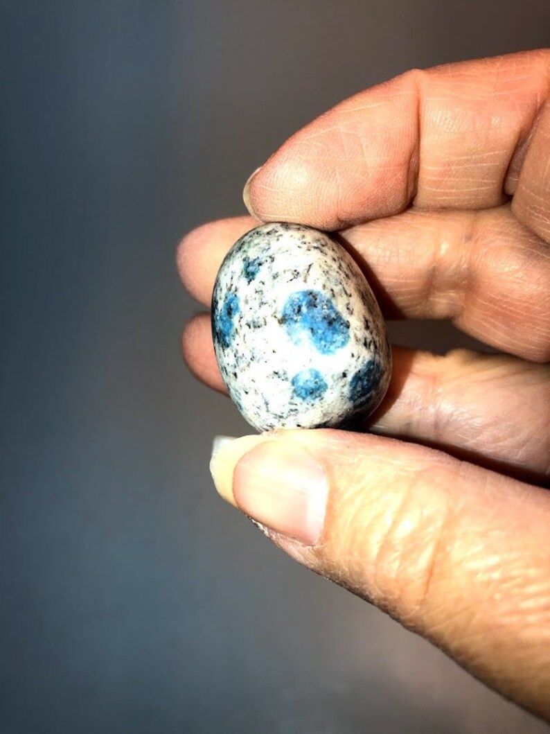 May include: A smooth, oval-shaped blue and white kyanite stone with a speckled pattern.