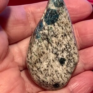 May include: A smooth, teardrop-shaped stone with a white, gray, and blue marbled pattern. The stone has a glossy finish and is speckled with small, dark blue flecks.