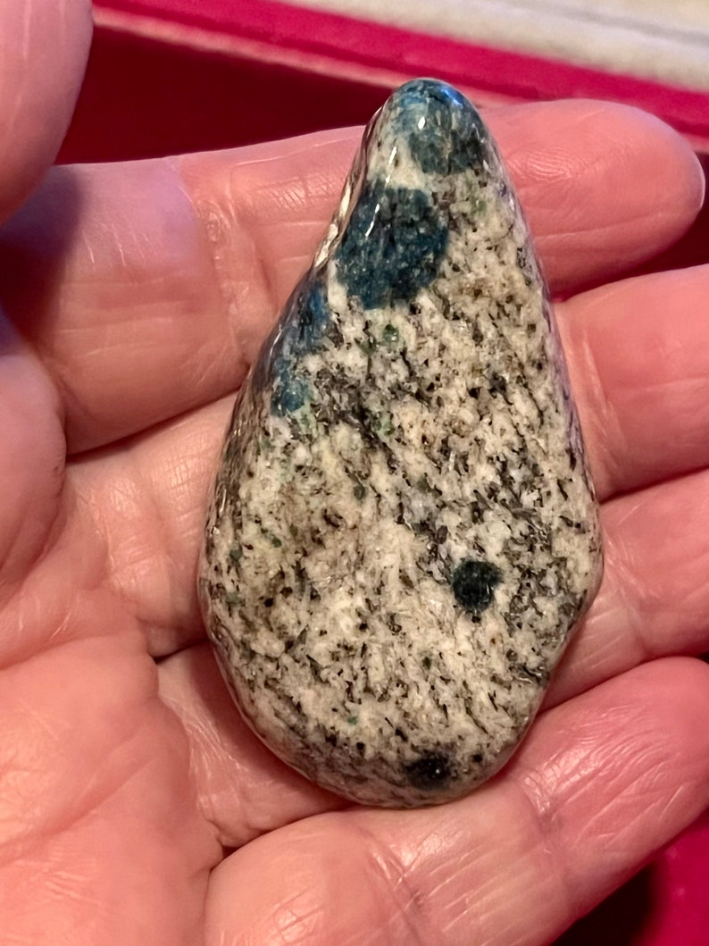 May include: A smooth, teardrop-shaped stone with a white, gray, and blue marbled pattern. The stone has a glossy finish and is speckled with small, dark blue flecks.