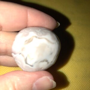 May include: A white agate stone with gray and brown swirls and patterns.