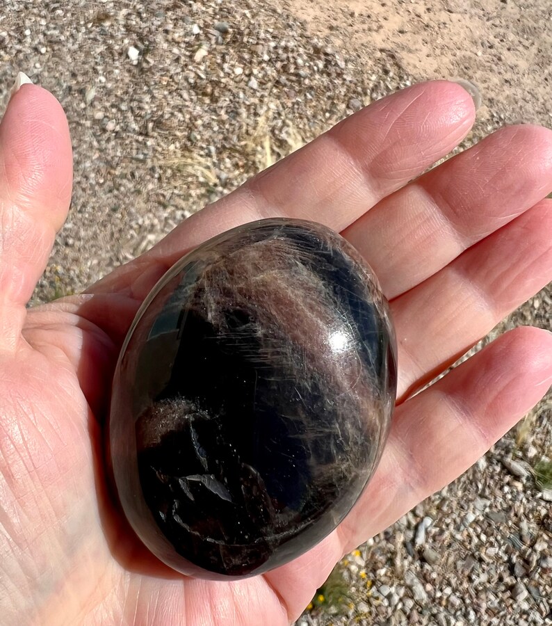 May include: A smooth, black and brown gemstone sphere with a high polish. The sphere is about the size of a golf ball.