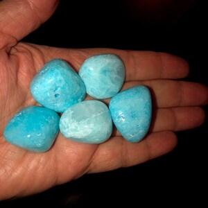 May include: Five smooth, light blue tumbled stones, likely aquamarine, in a hand.