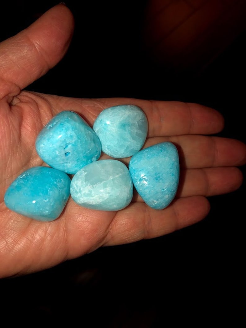 May include: Five smooth, light blue tumbled stones, likely aquamarine, in a hand.