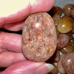 May include: A smooth, translucent, light brown and pink tumbled stone with a white, cloudy interior. The stone has a rough, textured surface.