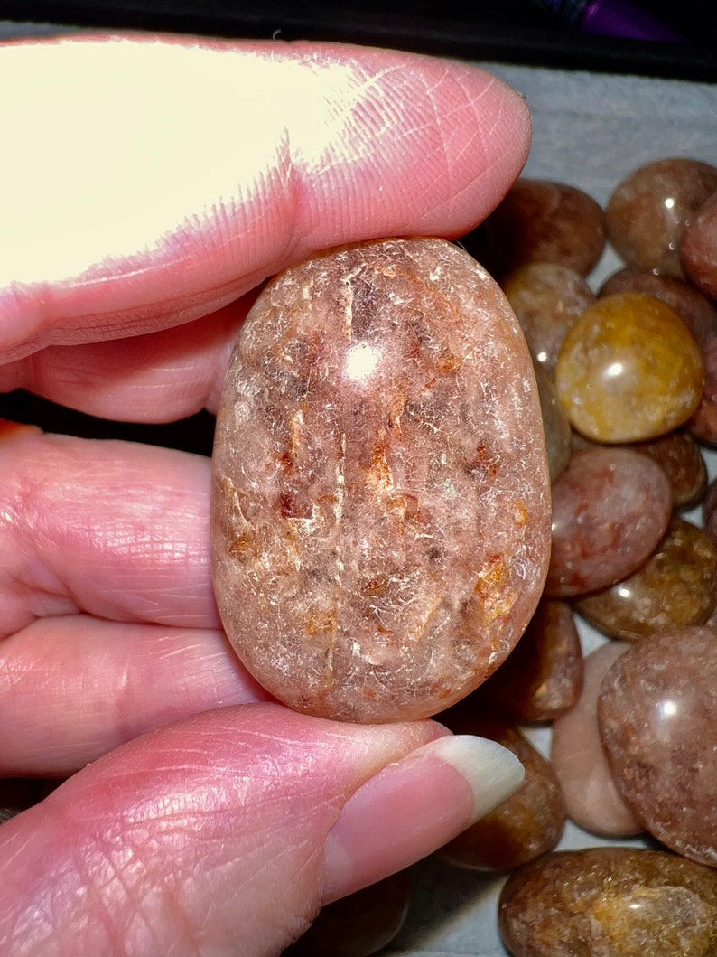 May include: A smooth, translucent, light brown and pink tumbled stone with a white, cloudy interior. The stone has a rough, textured surface.