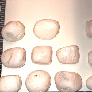 Op de afbeelding: Een verzameling van tien roze en witte getrommelde stenen. De stenen zijn glad en hebben verschillende vormen en maten.