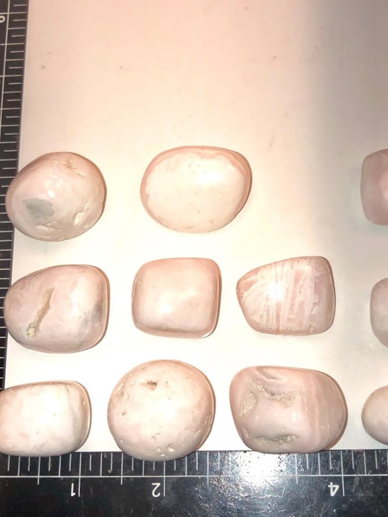 Op de afbeelding: Een verzameling van tien roze en witte getrommelde stenen. De stenen zijn glad en hebben verschillende vormen en maten.