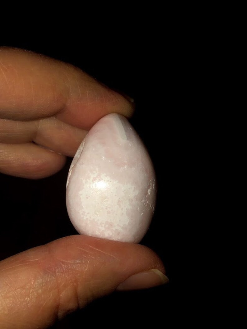Op de afbeelding: Een glad, wit, eivormig kristal met roze en witte swirls. Het kristal is ongeveer zo groot als een groot ei.