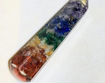 May include: A clear, rectangular crystal wand filled with layers of colorful stones. The stones are arranged in bands of red, yellow, green, blue, and purple. The wand is approximately 5 inches long.