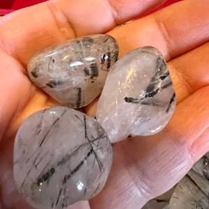 Puede incluir: Tres piedras pulidas de cuarzo transparente con inclusiones de turmalina negra. Las piedras son lisas y pulidas, y tienen una forma natural y org&aacute;nica.
