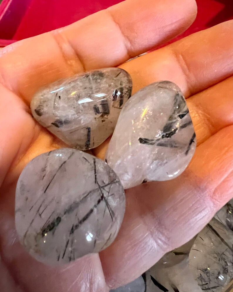Puede incluir: Tres piedras pulidas de cuarzo transparente con inclusiones de turmalina negra. Las piedras son lisas y pulidas, y tienen una forma natural y org&aacute;nica.