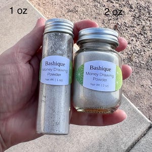 May include: Two glass jars with silver lids containing a light gray powder. The jars are labeled "Bashique Money Drawing Powder" with the net weight of 1 oz and 2 oz.