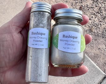 May include: Two glass jars with silver lids containing a light gray powder. The jars are labeled "Bashique Money Drawing Powder" with the net weight of 1 oz and 2 oz.