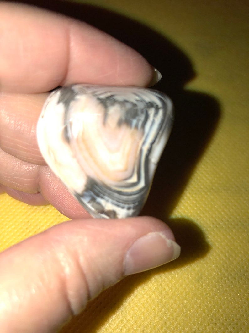 May include: A close-up of a white and black banded agate stone with a pink center. The stone is smooth and polished.