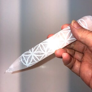 May include: White selenite crystal wand with a carved flower of life design. The wand is approximately 6 inches long.